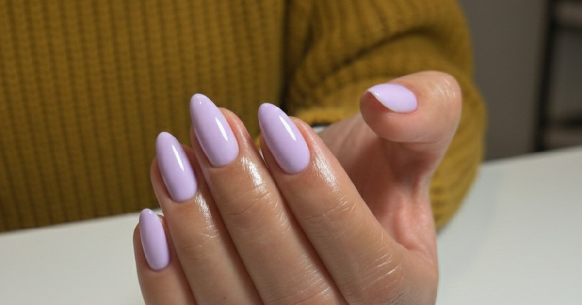 A close-up of a hand with long, almond-shaped pastel lavender nails, wearing a diamond ring and a mustard yellow knit sweater.